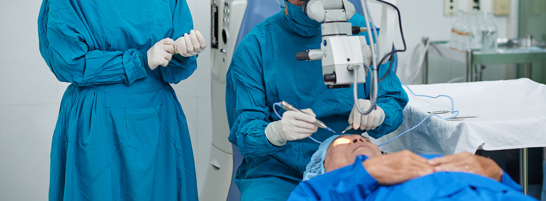 In the image, two individuals wearing medical gowns and masks are examining an object on a table, with one person operating a device while the other observes.