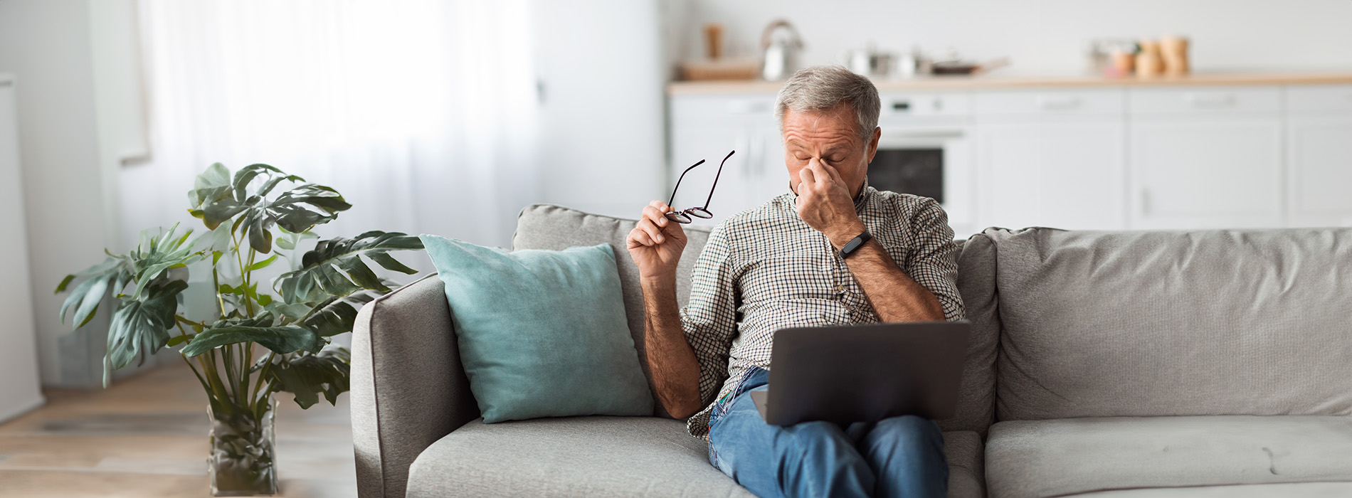 An elderly man sitting on a couch with his eyes closed, wearing glasses, and holding a piece of paper.