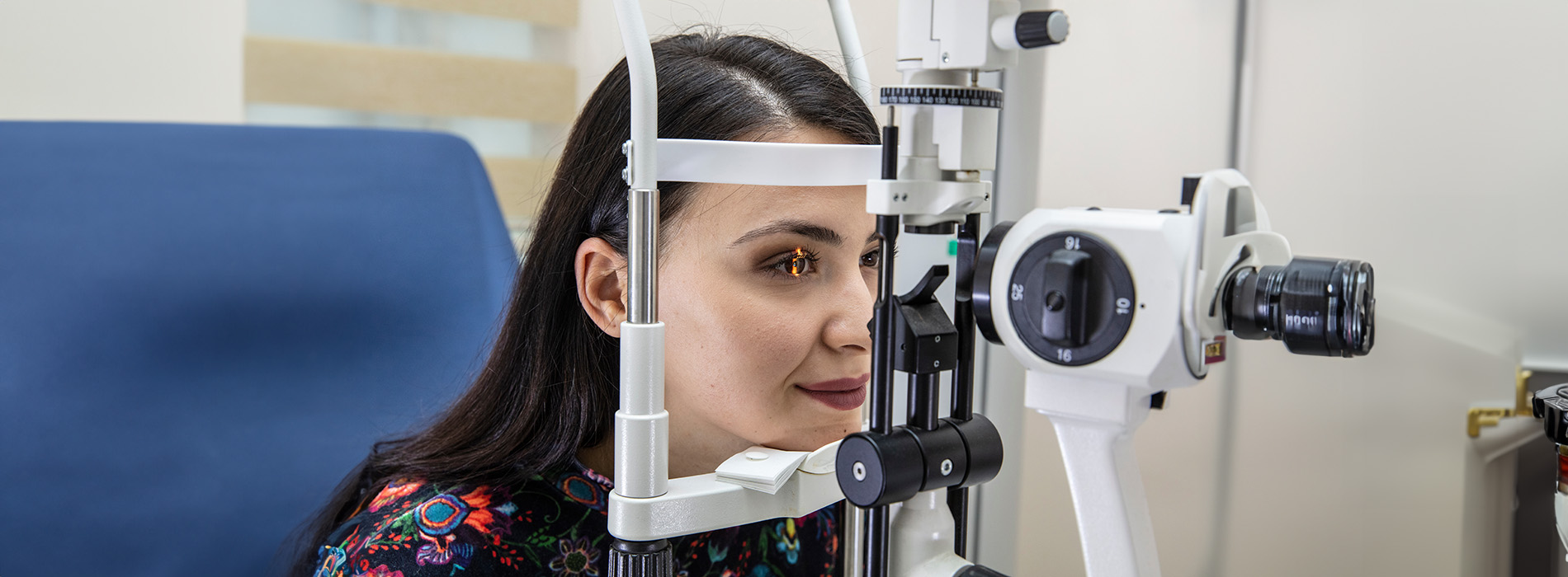 A woman seated at an ophthalmology examination machine, looking through a device with a focused expression.