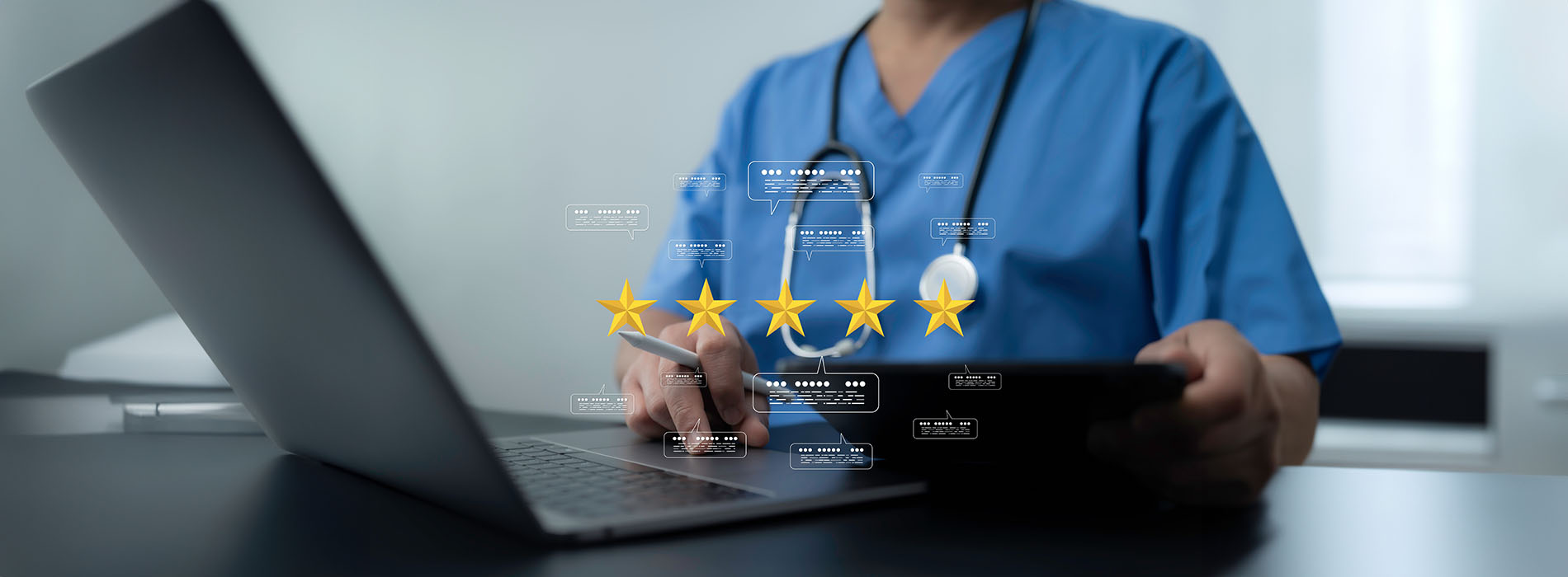 The image shows a professional setting with a person in a medical uniform working on a laptop while surrounded by various work-related items, including a mouse and a coffee cup.